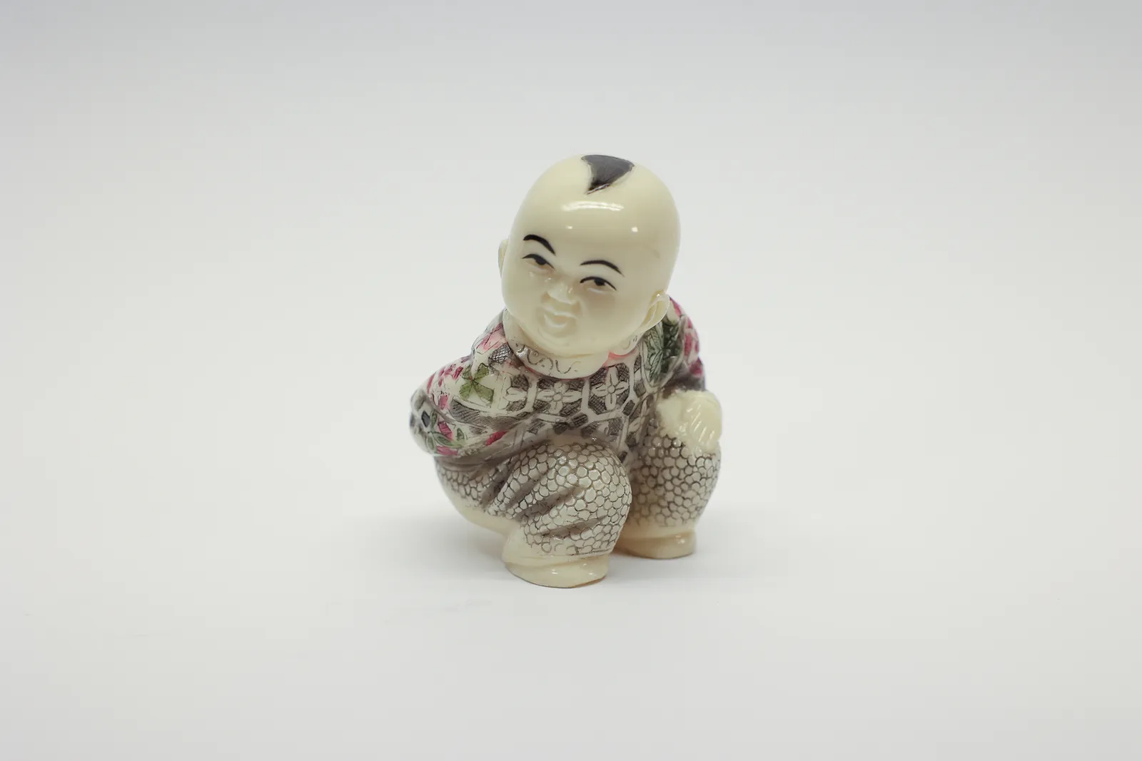 Carved Figural Squatting Child in Floral Robe